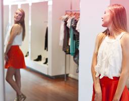 Ung kvinde stående foran et spejl og forsøger nyt tøj. Billede illsutrerar hvordan en ung kvindes krop ændrer sig i puberteten.