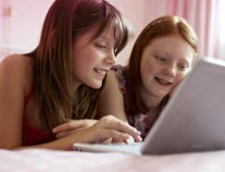Billede af to unge piger sidder foran en computer. Billedet illustrerer, at det er almindeligt at have mange spørgsmål og ob® hjemmeside kan du finde information om den første menstruation, pubertet og andre nyttige oplysninger.